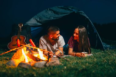 Gece kamp yapan romantik bir çift, kamp ateşinde ızgara sosis ve arkadaşlığın tadını çıkarıyorlar.