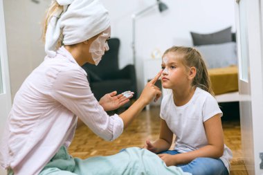 Anne evde kızına kozmetik maske takıyor.