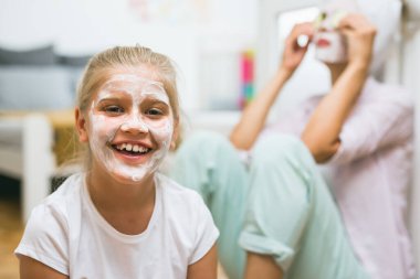 Yüzünde kozmetik maske olan bir kıza yaklaş. anne arka planda bulanık