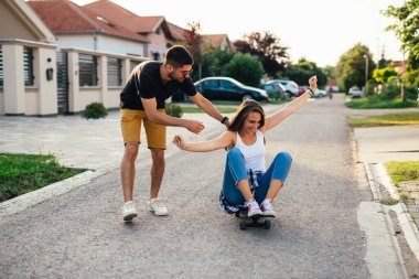Genç çift dışarıda kaykay sürerken eğleniyor.