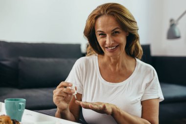 Orta yaşlı bir kadın evinde oje sürüyor.