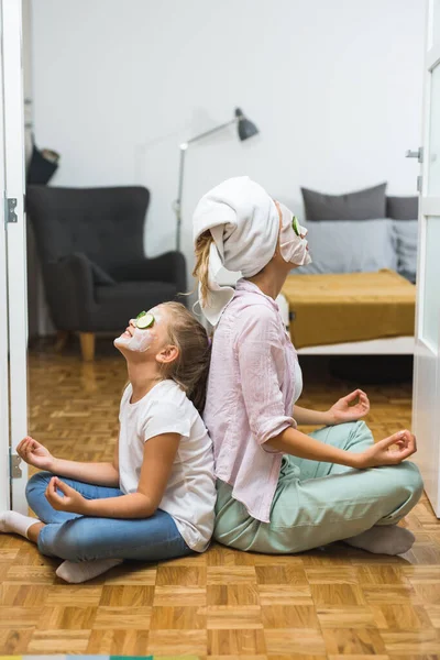 mother and daughter meditating at home with cosmetic face mask applied