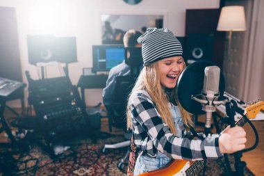 Kız müzik stüdyosunda şarkı söylüyor ve gitar çalıyor.