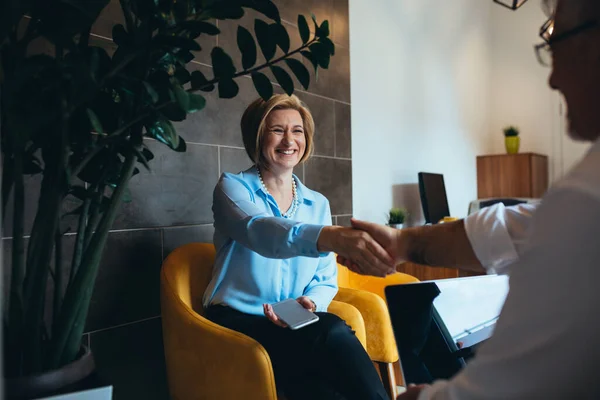 Kadın emlakçı müşteriyle tokalaşıyor.