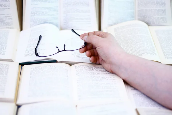 Bir adam ile okuma gözlüğü açık bir kitap üzerinde bir el ile bir kitap okur.