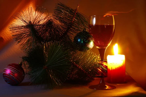 Yeni yılki tatil natürmort bir kadeh şarap, bir Noel ağacı ve bir mum Noel süslemeleri ile alev.
