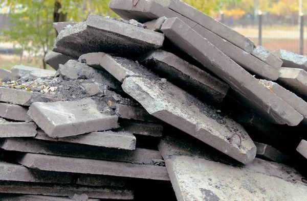 A large pile of broken, gray biton slabs lies on the ground. Construction of the road in the city