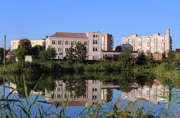 Painting of buildings that are reflected in the water at the lake. Vokruk grows grass and trees. Rest outside the city