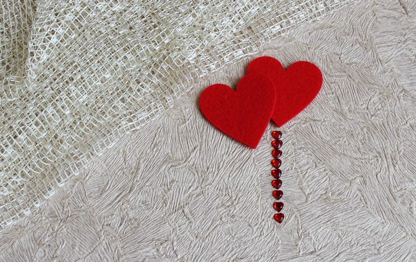 Two red hearts on a light background, which is divided by a cloth. Near a strip of small glass hearts