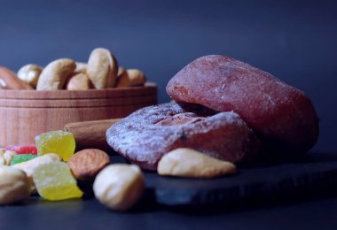 Parlak şekerlenmiş meyve, fındık ve Trabzon hurması kurutulmuş. Karanlık bir arka plan karşı bir tabakta yemiş/kuru meyveler yalan.