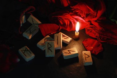 Poşetteki ahşap mühürler, kırmızı güllerin yapraklarının etrafında, yakınlarda bir mum yanıyor. Mumların arkasında bir buket kırmızı gül var..