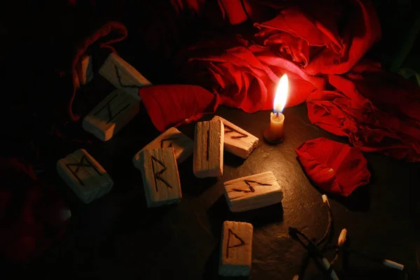 View of the mystical composition of wooden runes around the petals of red roses, a candle burns next to it and the burnt matches lie. — Stock Photo, Image