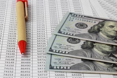 Kırmızı kalem ve Amerikan doları para numaraları olan bir masanın üzerinde yatıyor. Para kavramı. Bankacılık, yatırımlar, mevduat, tasarruf. Arka planı bulanıklaştırma