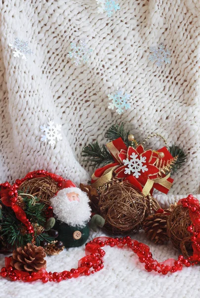 Weihnachtsspielzeug, Weihnachtsmann, rote Perlen und Zweige eines Weihnachtsbaums auf weißem Strickgrund, an dem Schneeflocken hängen — Stockfoto