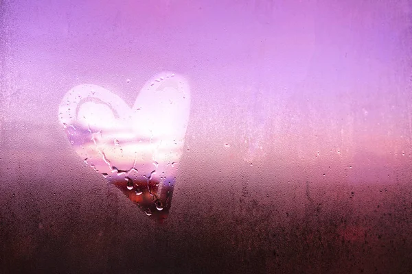 Heart shape on fogged window glass. Love concept. Beautiful pink sunset sky, steamy window glass surface