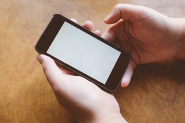 Ahşap arka planda beyaz boş ekranlı cep telefonu kullanan eller, kapatın. Kopyalama alanı