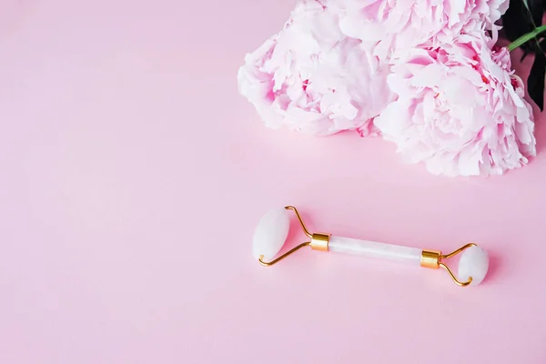 Jade stone roller made of pink quartz on pink background.