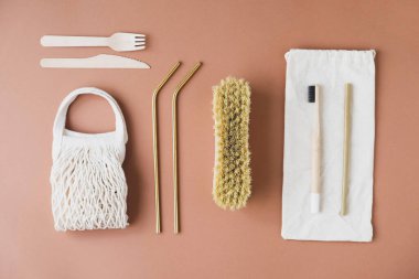 Kahverengi arka planda yeniden kullanılabilir çevre dostu öğeler. Pamuklu ağ torbası, metal pipet, doğal fırça, bambu diş fırçası, ahşap çatal bıçak takımı. Sıfır atık, plastiksiz ve sürdürülebilir yaşam tarzı kavramı. 