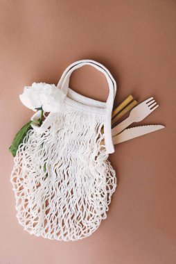 Yeniden kullanılabilir çevre dostu pamuk örgü torbası bambu içerek pipet, ahşap çatal bıçak takımı ve kahverengi arka planda çiçek. Uzayı kopyala, üst görünüm. Sıfır atık, plastik yok, sürdürülebilirlik. Yaz pikniği kavramı.