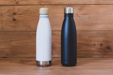 Yeniden kullanılabilir çevre dostu siyah ve beyaz paslanmaz çelik termo şişeler ahşap kırsal arka planda. Uzayı kopyala Sıfır atık, plastik yok, sürdürülebilirlik. Kendi su şişesi konseptini getir..