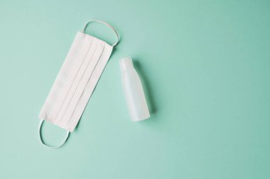 Antiseptik jel şişesi ve pastel yeşil arka planda koruyucu yüz maskesi. Uzayı kopyala Kişisel hijyen, sağlık ve Coronavirus Covid-19 önleme.