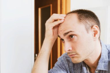 Aynaya bakan genç adam kelleşmeyi dert ediyor..