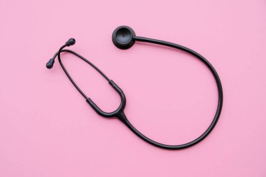 Pastel pembe arka planda siyah modern steteskop. Tıp ve sağlık, kardiyoloji, tıp eğitimi. Akustik tıbbi cihaz. Mesaj için yer var. Düz-yatay, üst görünüm.