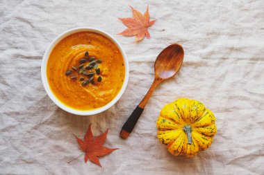 Beyaz masa örtüsünde kabak tohumlarıyla servis edilen sıcak balkabağı çorbası, üst manzara, düz yatak. Ev yapımı sonbahar yemekleri. Popüler Şükran Günü yemeği..