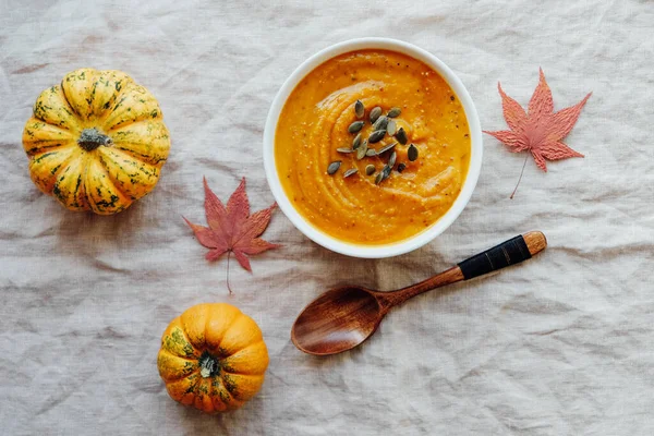 Hot pumpkin soup served with squash seeds in a bowl on white tablecloth background, top view, flat lay. Homemade autumn food. Popular Thanksgiving dish.