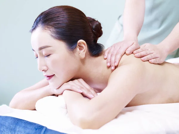 side view of a beautiful young asian woman receiving massage in spa salon, eyes closed.