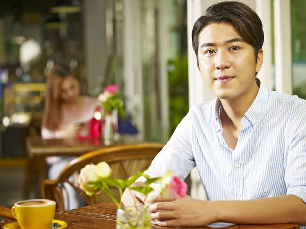 年轻的亚裔男子坐在咖啡店或茶馆的桌子上与一个年轻的妇女在背景 — 图库照片