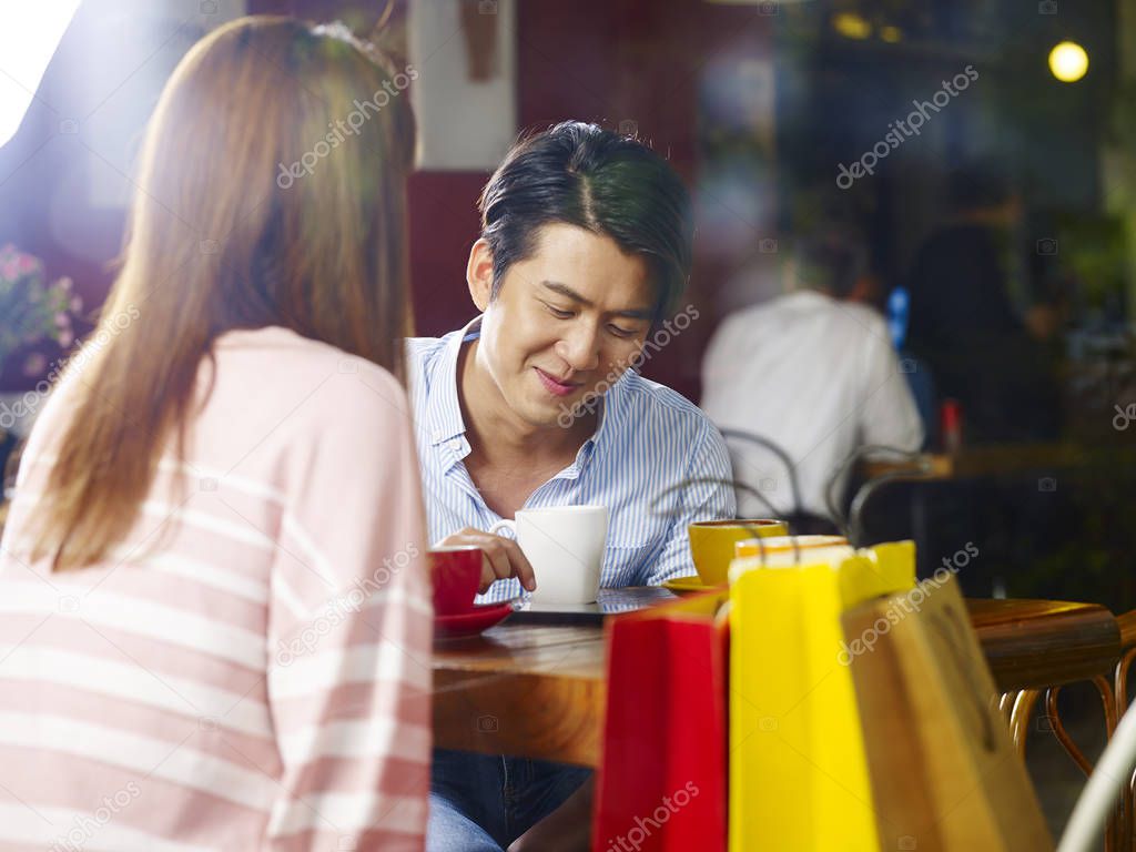 young asian couple relaxing chatting talking in coffee shop after shopping, shot through window glass.