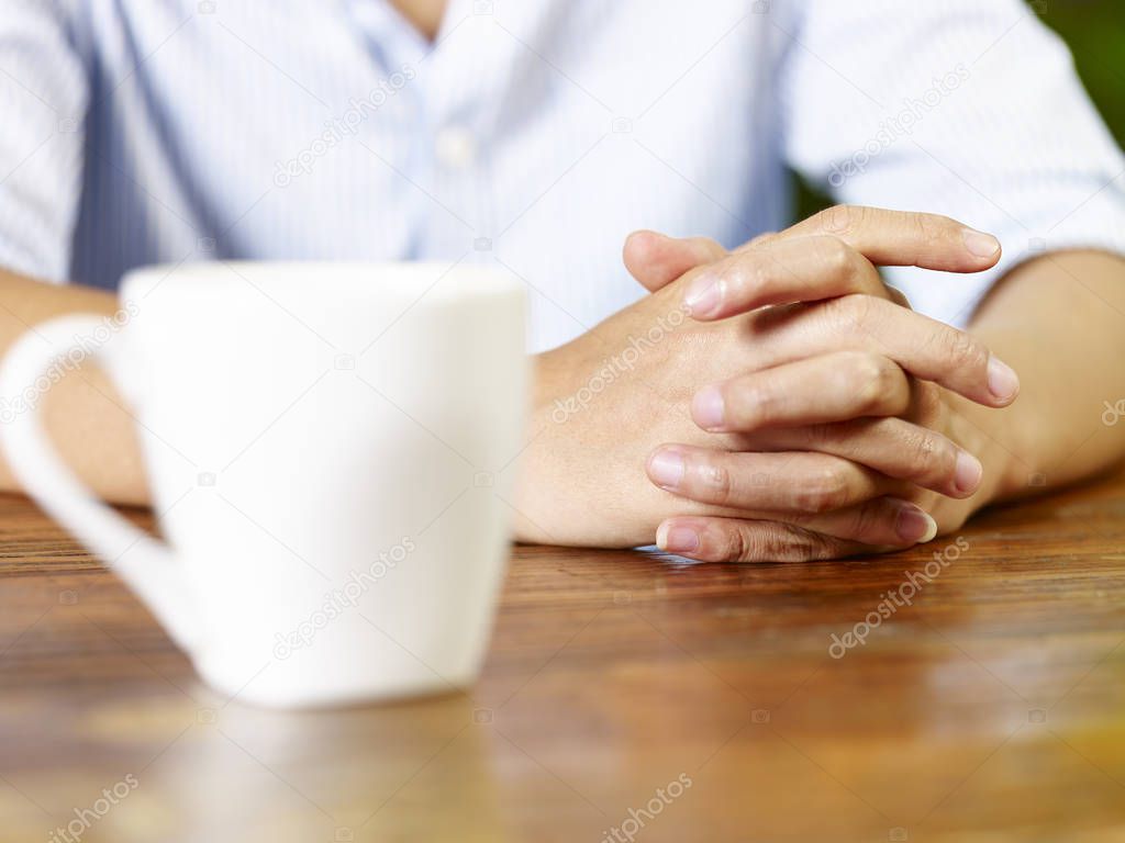 hands of a young man and a white mug on wooden table in coffee shop or tea house.