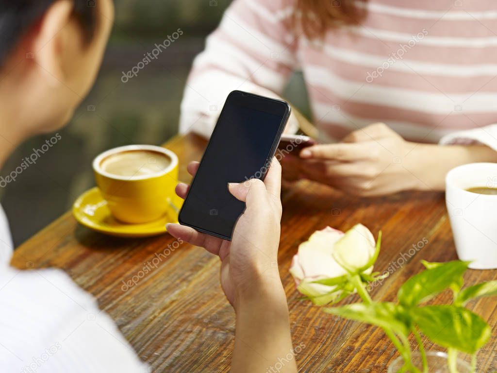 young asian man and woman sitting face to face in coffee shop using mobile phone.