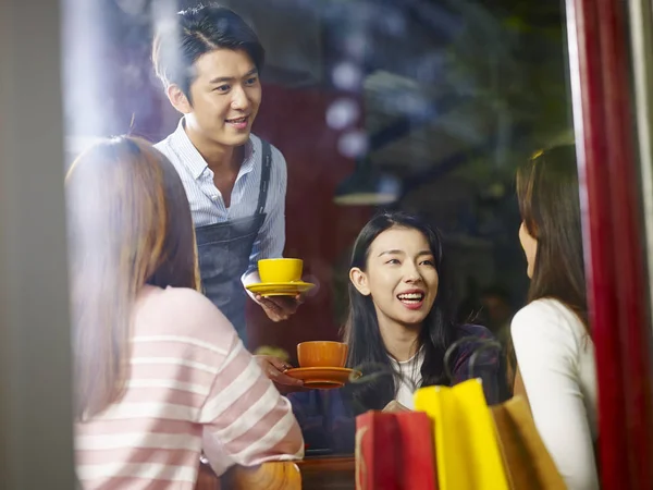 Genç Asyalı garson kahve dükkanı, kadın müşterilerine hizmet pencere camı delip vurdu.