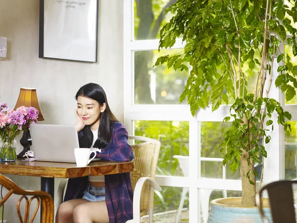 dizüstü bilgisayar kullanan kahve dükkanı çalışma köşesinde oturan güzel genç Asyalı kadın.