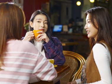 Tablo sohbet kafe veya çay evi konuşurken oturan üç mutlu güzel genç Asyalı kadınlar.