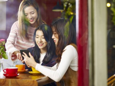 konuşan sohbet masada oturan üç mutlu güzel genç Asyalı kadın kahve dükkanı veya çay evi, cep telefonu ile oynarken pencere camı delip vurdu.