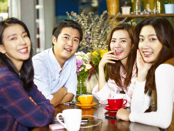 つの幸せなアジアの若い大人の男とコーヒー ショップで収集しながら笑みを浮かべてカメラを見ている女性のグループ — ストック写真