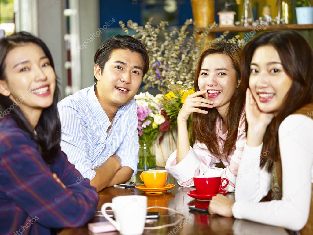 group of four happy asian young adults man and woman looking at camera smiling while gathering in coffee shop.