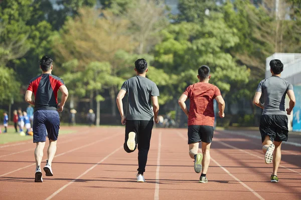 young asian adult athletes running training on track, rear view.