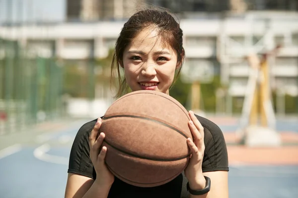 young asian woman holding a basketball looking at camera smiling.
