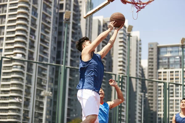 young asian basketball player going up for a layup while opponent playing defense.