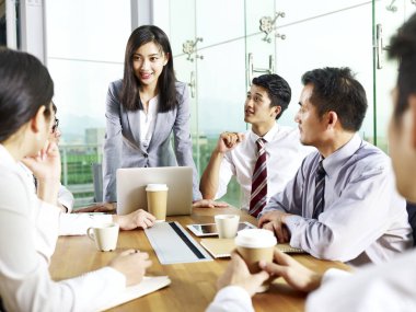 young asian businesswoman speaking to teammates during meeting in modern office. clipart
