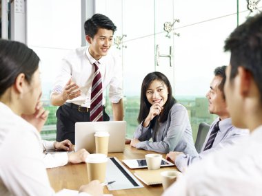 young asian businessman speaking to coworkers during meeting in modern office. clipart