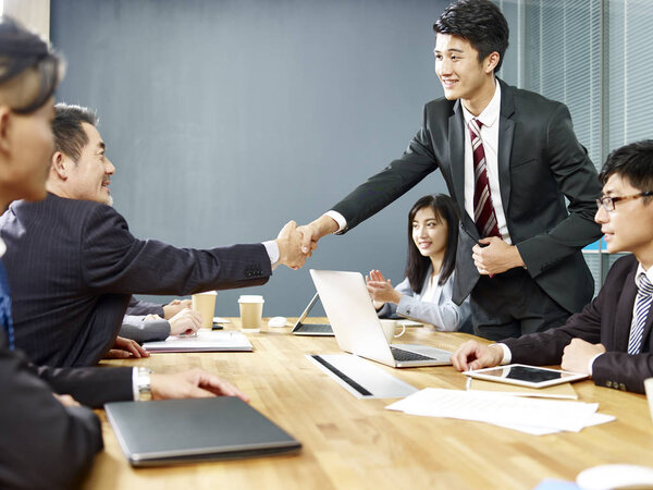 два азиатских руководителя корпораций пожимают друг другу руки за столом переговоров
.