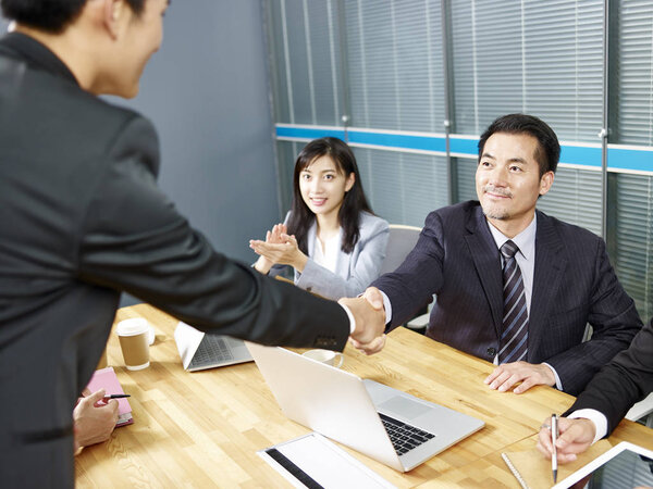 два азиатских руководителя корпораций пожимают друг другу руки во время встречи в офисе
.