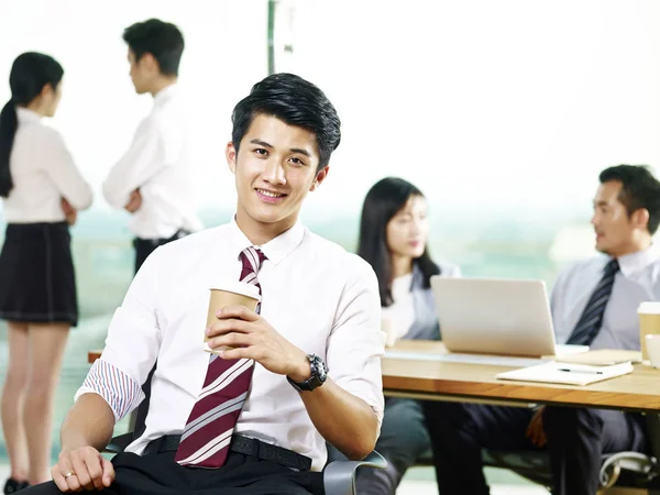 portrait of successful young asian corporate executive holding a cup of coffee looking at camera smiling in office.