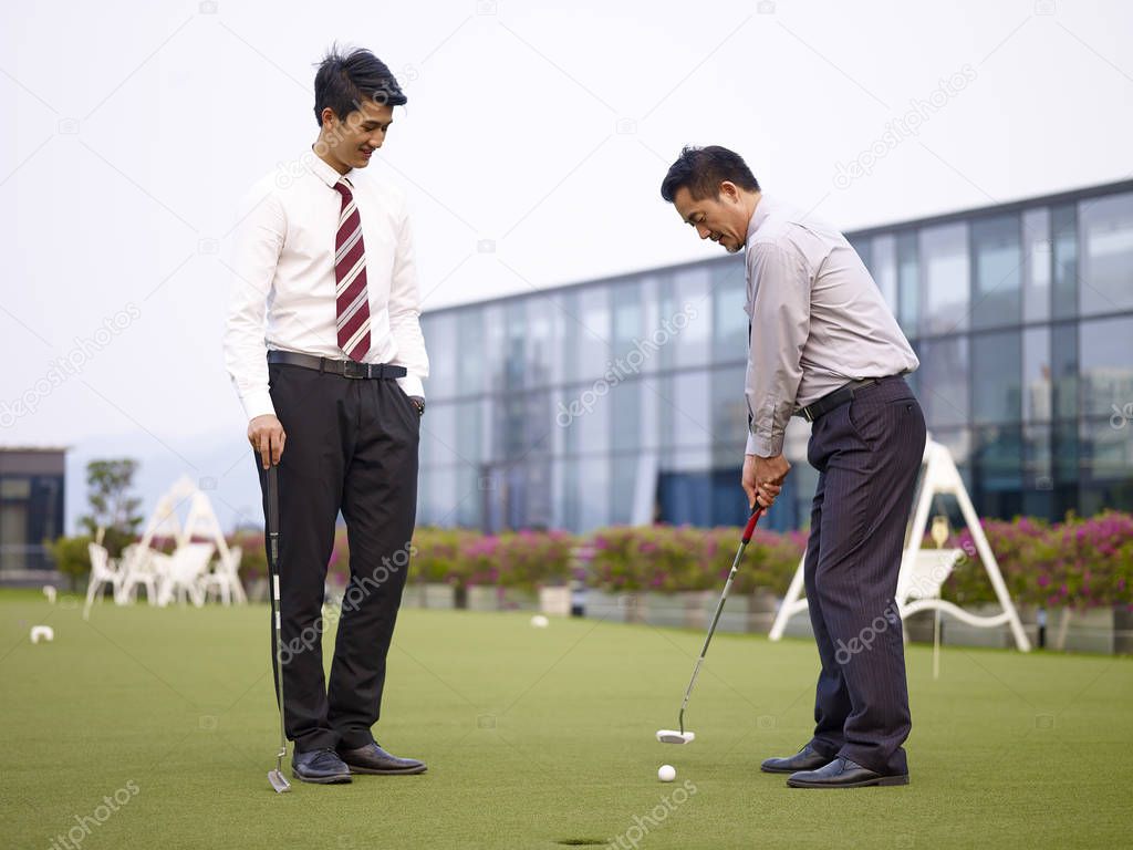 two asian business men relaxing and playing golf on rooftop court.