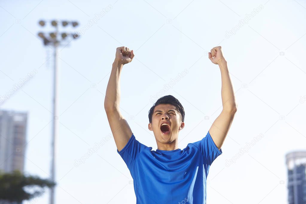 young asian male athlete celebrating victory with fists and arms raised